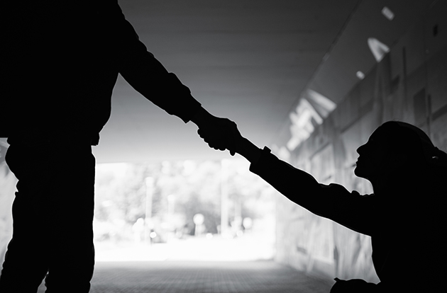 Standing person reaching down to person sitting on the ground